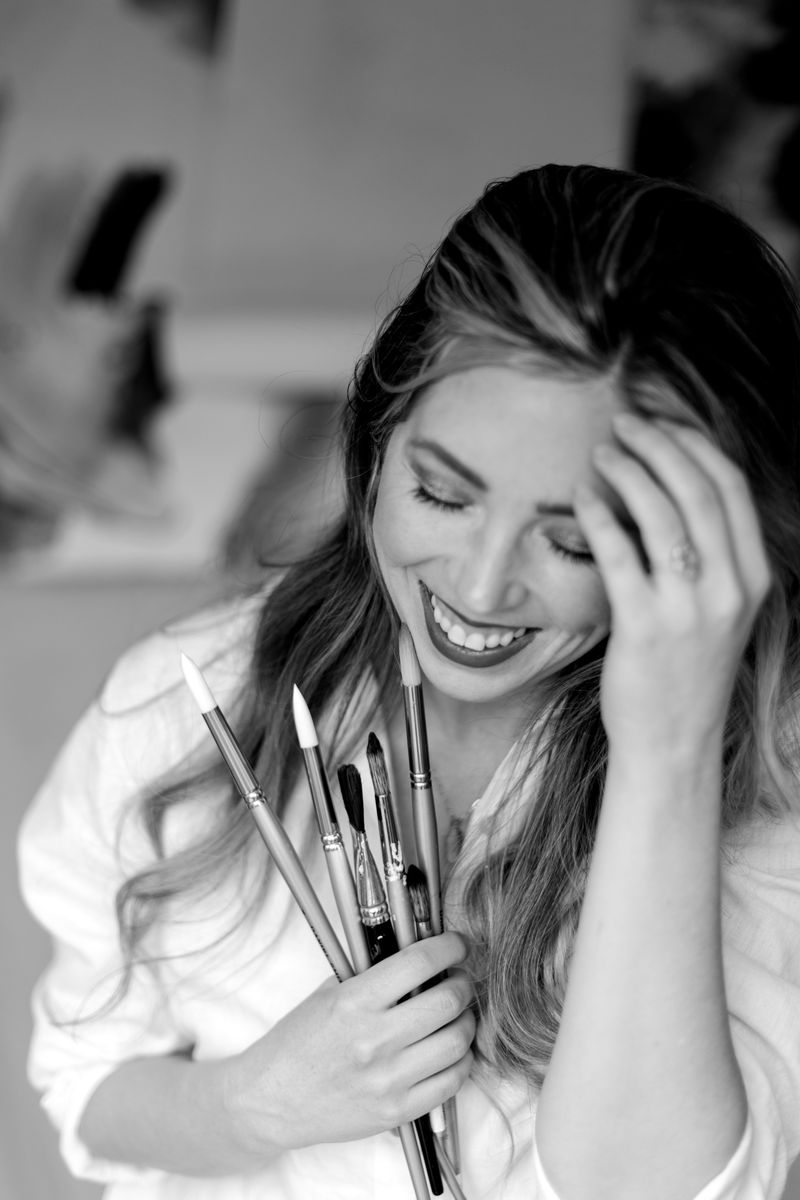 McKenna laughing in her studio, a handful of paintbrushes gathered against her