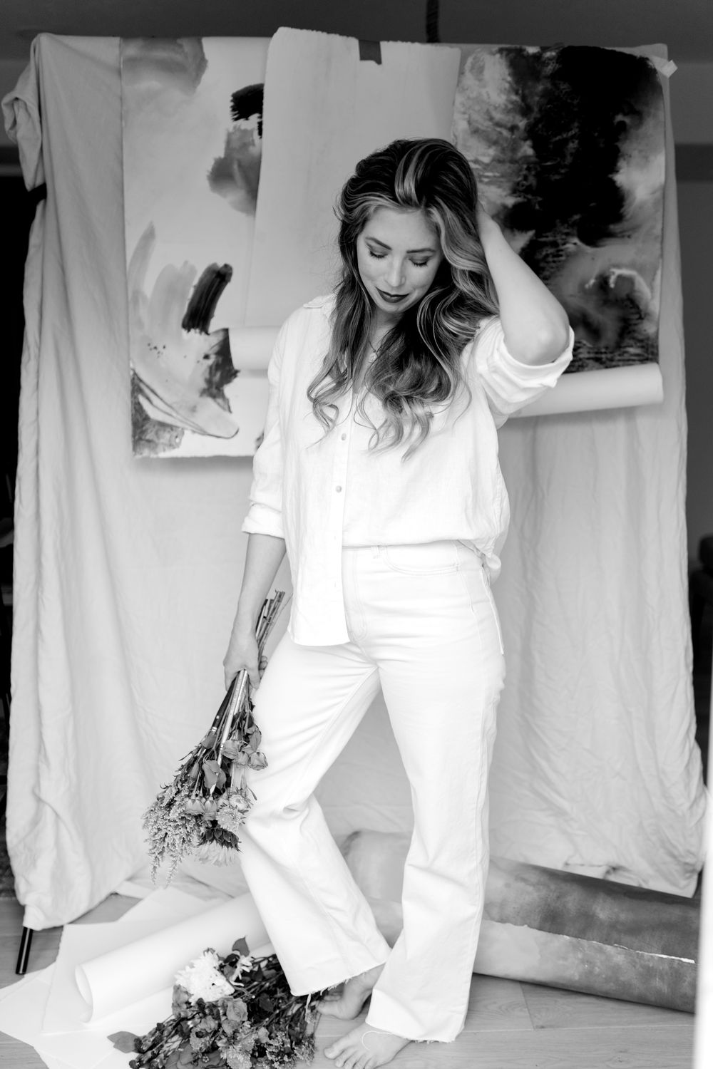 McKenna standing among painted canvases and studio drapes, dressed in white
